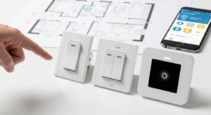 Vista superior de una mano señalando una selección de tres tipos diferentes de interruptores de luz: uno básico, uno conmutador y uno inteligente táctil, con un plano de casa y un teléfono inteligente difuminados al fondo.